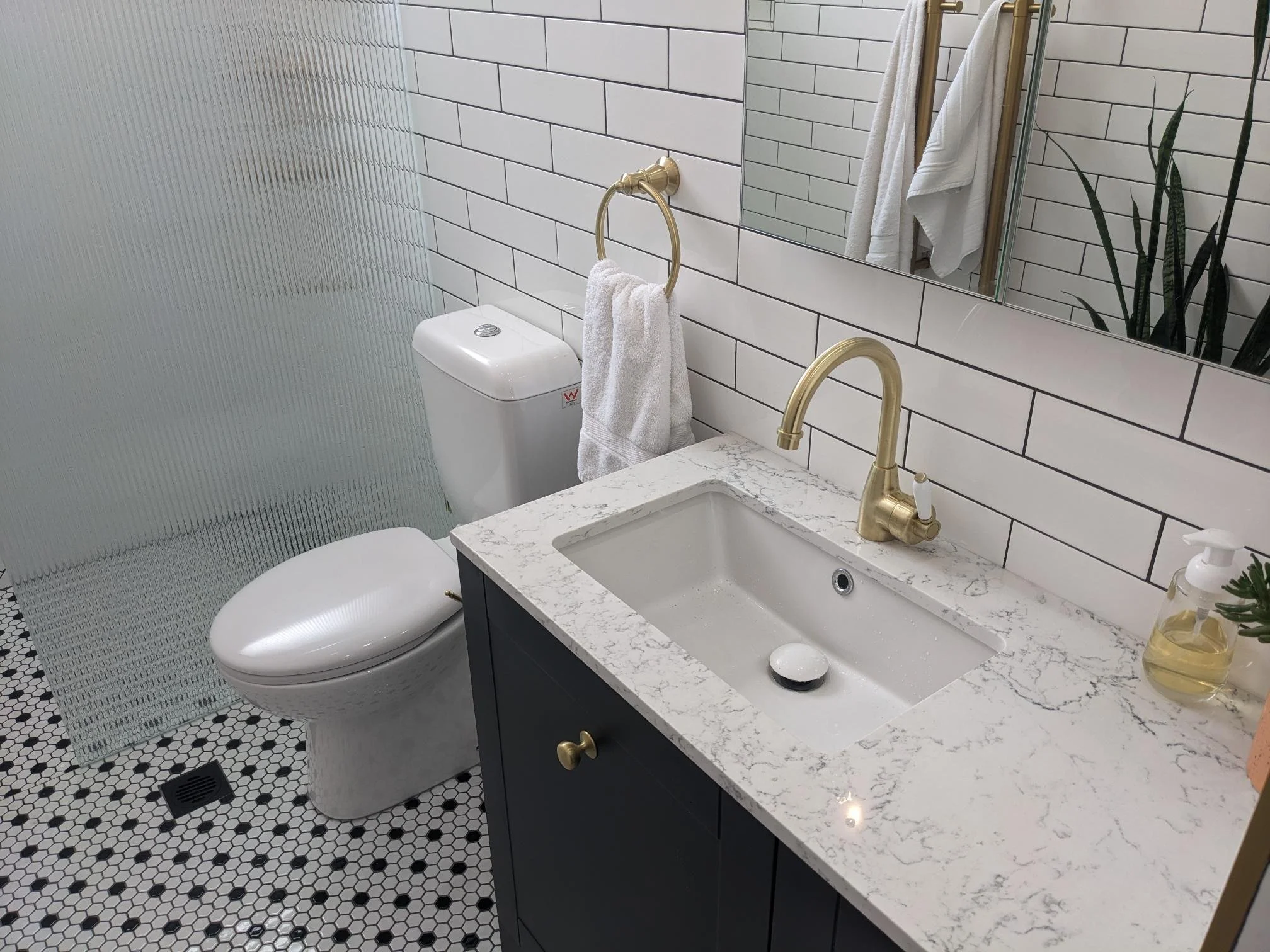 Sunshower bathroom renovation — dark vanity with marble benchtop, gold fixtures and hexagonal mosaic floor tiles
